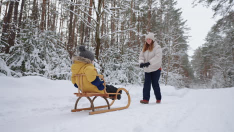 young-mother-and-little-son-are-riding-sledge-in-winter-forest-walking-between-high-snowy-spruces